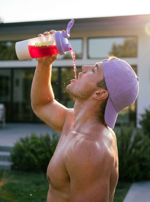 Man drinking Flowy from a shaker after training outdoors